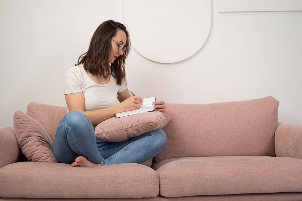 Kobieta siedząca na kanapie z notesem zapisująca swoje pomysły na biznes.